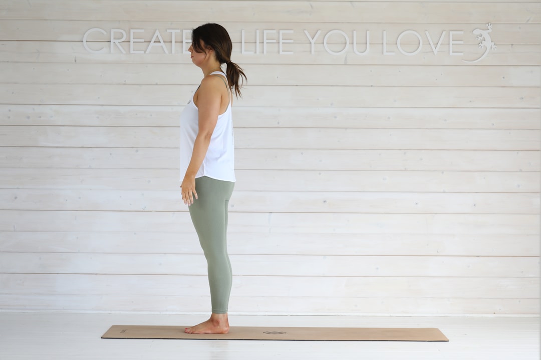 Woman standing on yoga mat in white tank top.