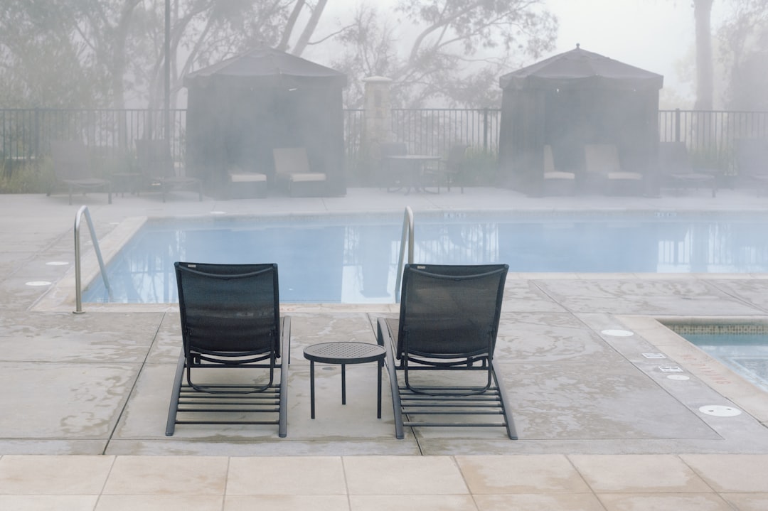 Two lounge chairs by a misty swimming pool.